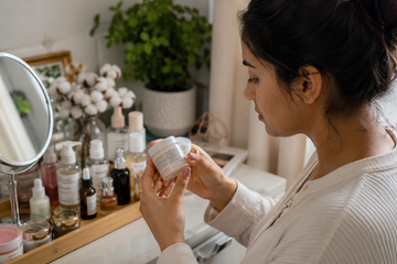 Woman checking a skincare product for signs of expiration at a bathroom vanity